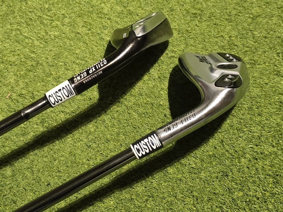 Two PXG 0311 GEN6 irons on turf with custom 3D-printed ferrules printed with the word CUSTOM