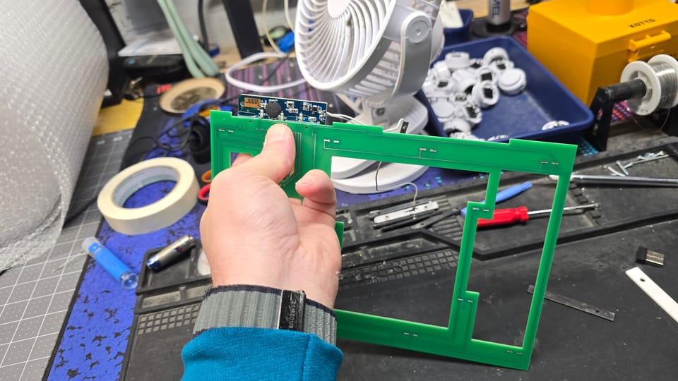 Bruce holding a green control box circuit board with the small wireless board attached, at the workbench